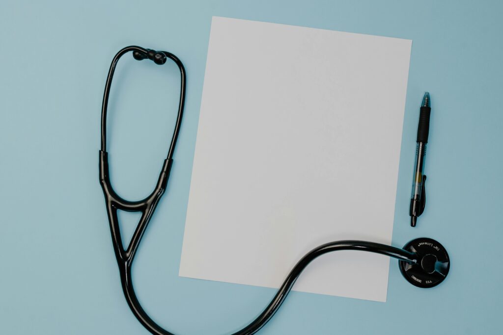 pexels-photo-7722676-7722676 Flat lay of a stethoscope, blank paper, and pen on a blue background.