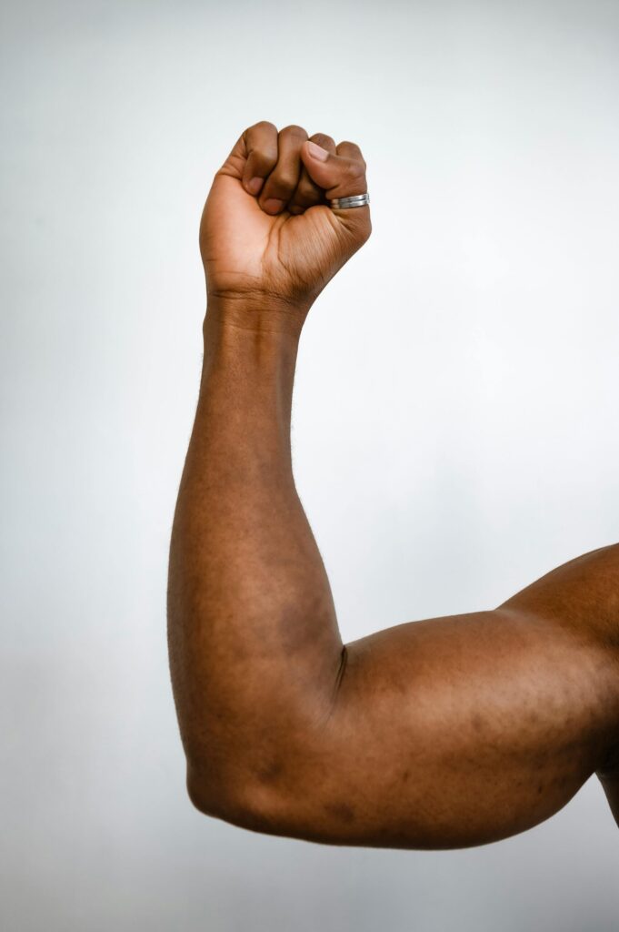 pexels-photo-8377227-8377227 Vertical shot of a muscular arm showing strength with a clenched fist.